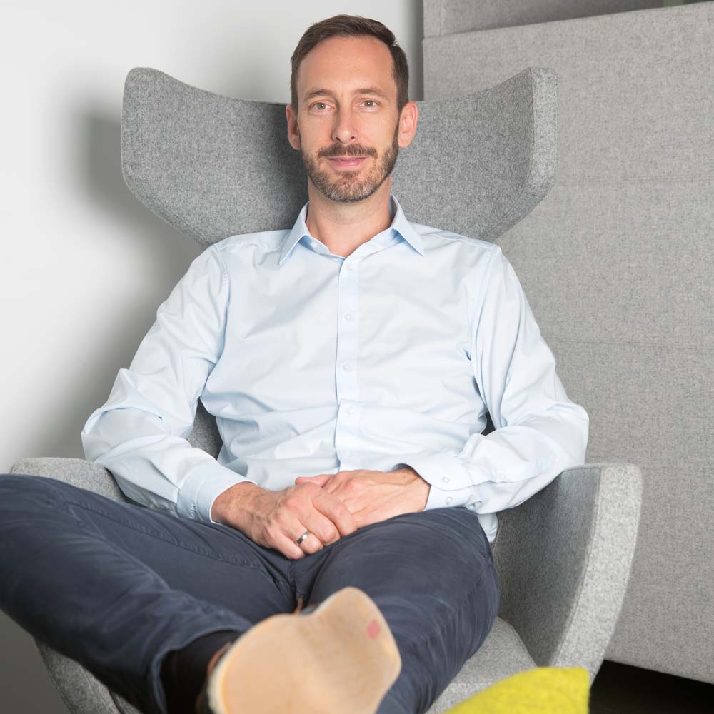 Ein Mann sitzt lächelnd in einem modernen Ohrensessel.