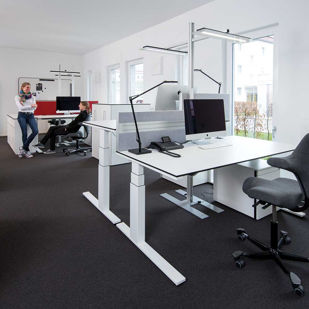 Ein helles Büro mit weißen Schreibtischen und zwei Frauen, die sich unterhalten.