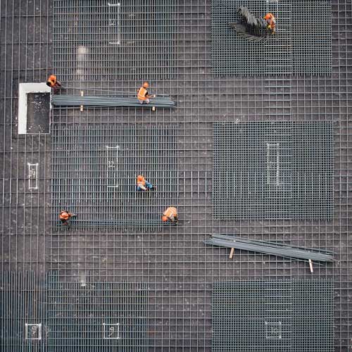 Sechs Bauarbeiter legen für das Fundament eines Gebäudes Metallstreben ineinander.