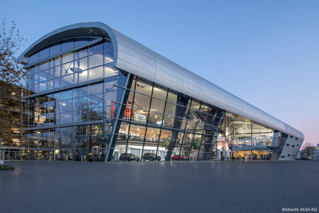 Audi Forum Neckarsulm – Außenansicht von der Piazza mit moderner Glasfassade und Besucherbereich